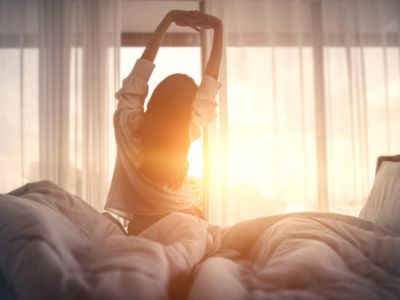 Mujer despertando y estirándose al amanecer en su cama.