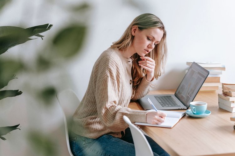 De aficionado a formulador: guía para crear tus propios productos capilares naturales con éxito Mujer estudiando un curso de formulación capilar natural online con un portátil y una libreta en casa
